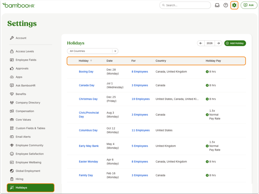 Screenshot of the Holidays section under Settings in BambooHR. The sidebar on the left lists navigation options such as Account, Access Levels, Employee Fields, and Holidays (highlighted in green). The main panel shows a table titled Holidays with columns for Holiday, Date, For, Country, and Holiday Pay. Holidays listed include Boxing Day, Canada Day, Christmas Day, Civic/Provincial Day, Columbus Day, Early May Bank, Easter Monday, and Family Day. Each row shows the date, number of assigned employees, applicable countries, and holiday pay information (e.g., “8 hrs” or “1.5x Normal Pay Rate”). The top-right area includes a green Add Holiday button and navigation arrows to change the year (currently set to 2026).